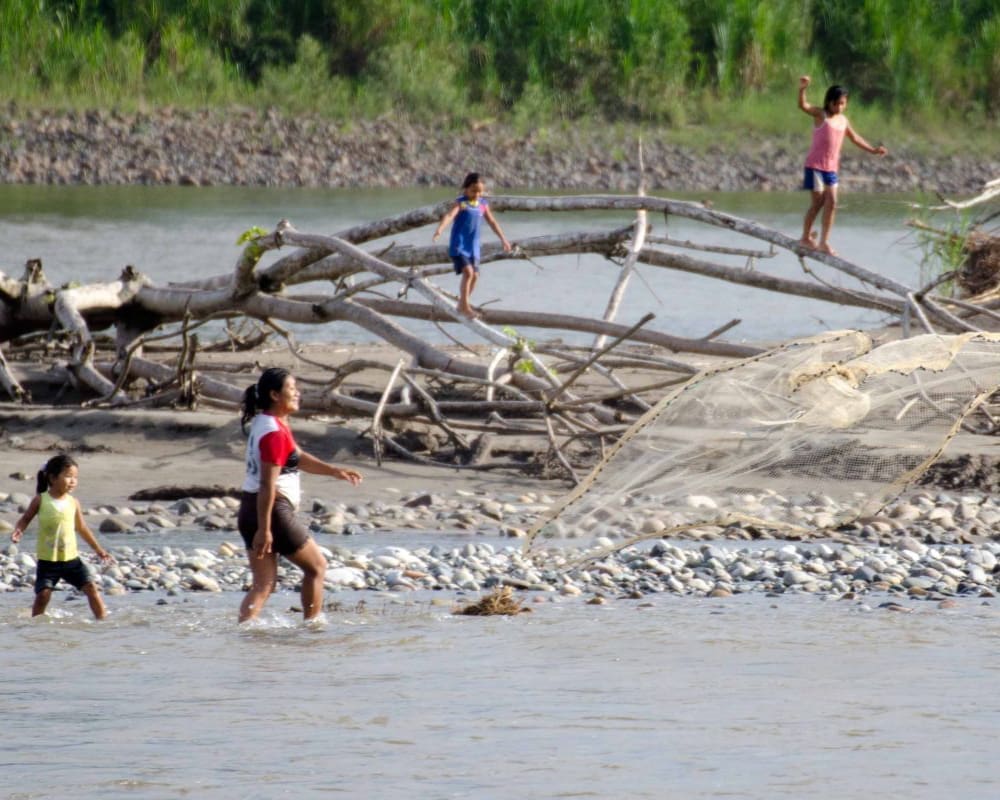 woman tosses a weighted fishing net into the river while her children play nearby